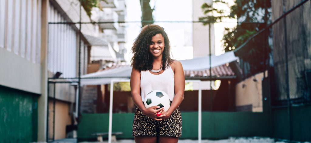 Young woman smiling and holding a soccer ball.
