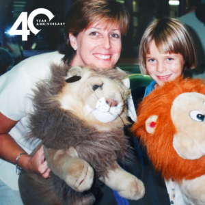 Vintage photo of Voices for Children founder Kathryn Ashworth smiling and holding lion toys with young girl