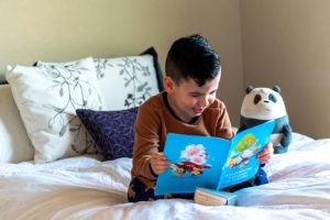 Young boy sitting on bed happily reading picture book