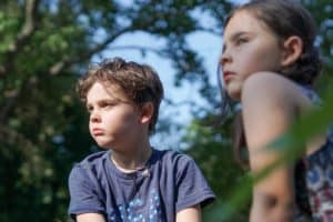 Boy and girl siblings sitting in grass staring away