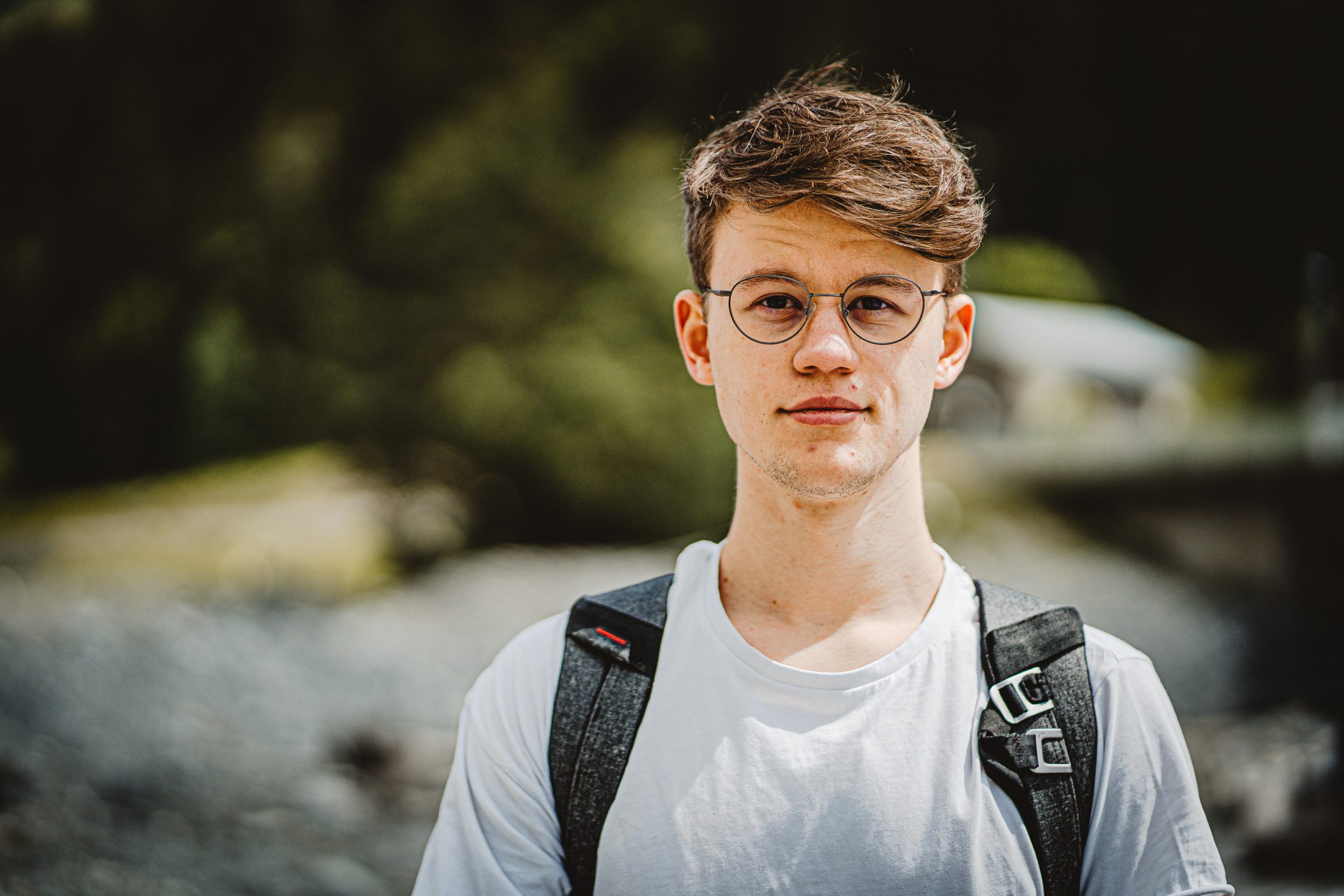 Teenage boy wearing glasses and backpack smiling at camera
