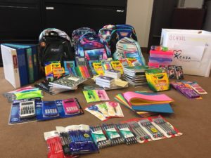 Pile of new school supplies including backpacks, colored pencils, markers, calculators, pens and pencils, combination locks, index cards, notebooks, and more.