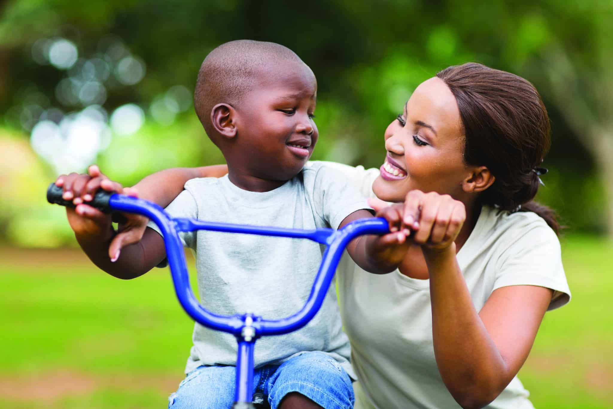 pretty young african woman helping her adorable son ride a bike